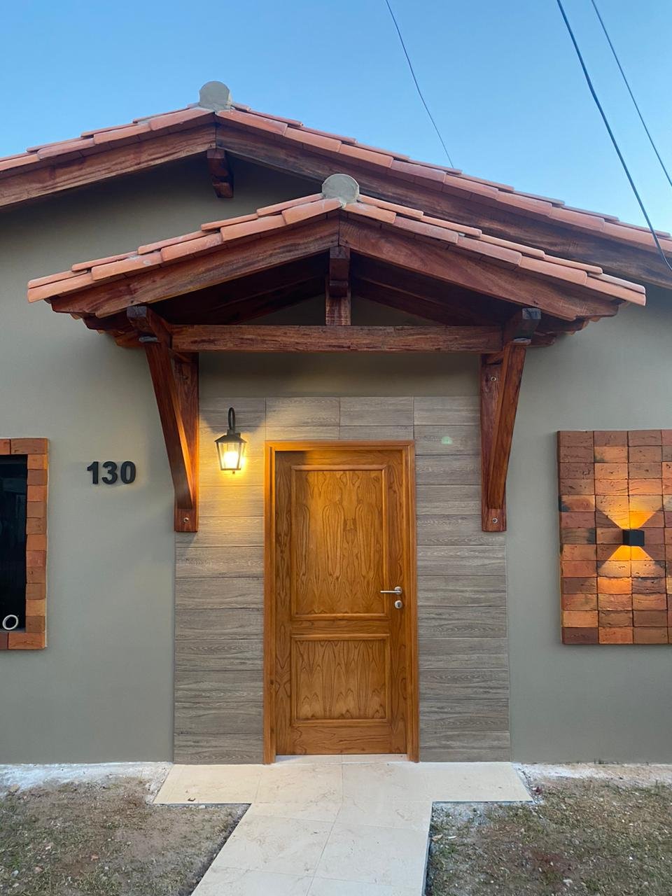 Frente renovado con puerta de madera y revestimiento simil piedra, San Lorenzo - OGA Constructora