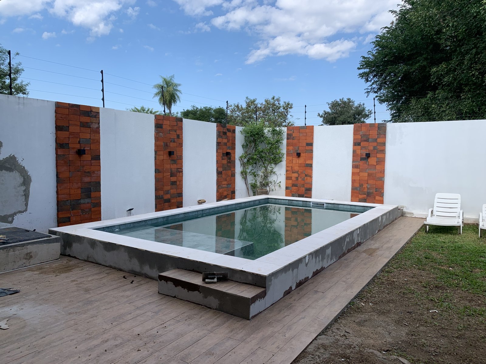 Piscina con muro decorativo de ladrillo y deck de madera, remodelacion en Loma Pyta - OGA Constructora