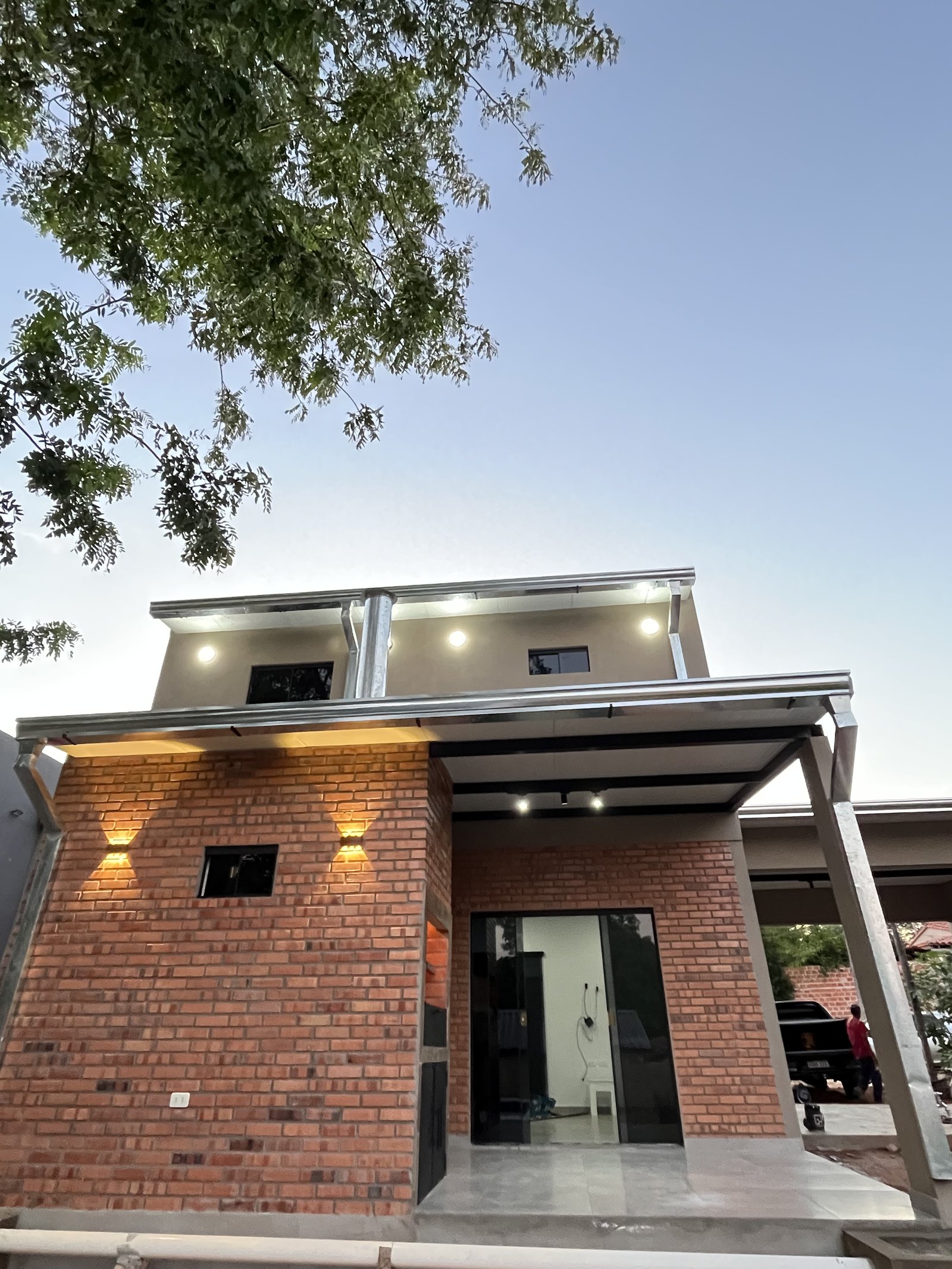 Fachada de vivienda de dos plantas en ladrillo visto iluminada al atardecer, San Lorenzo - OGA Constructora