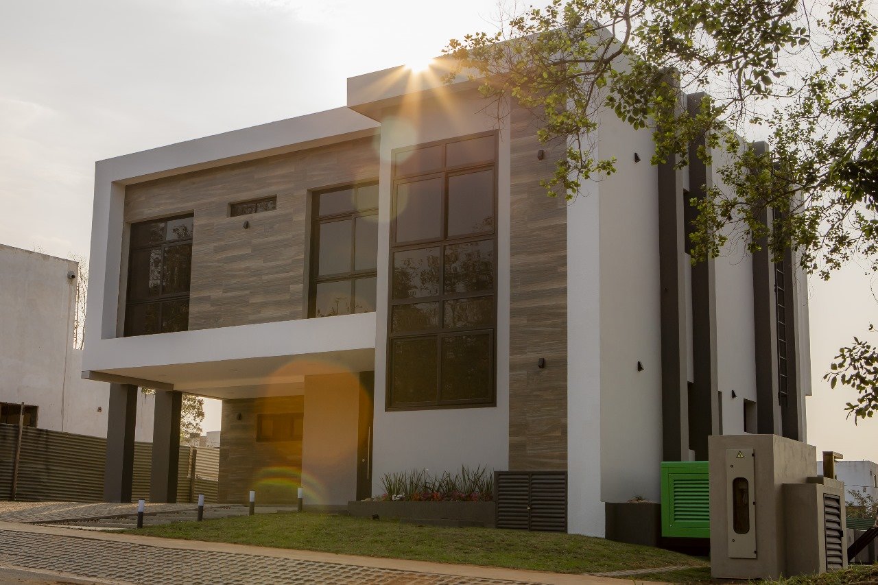 Fachada diurna de casa moderna de dos plantas con revestimiento de piedra y carpinteria de aluminio, Aqua Village - OGA Constructora