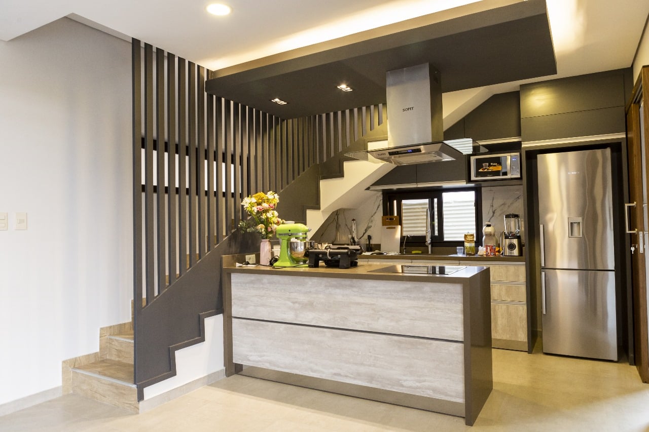 Cocina moderna con isla y escalera de hormigon, electrodomesticos de acero inoxidable, interior de vivienda Aqua Village - OGA Constructora