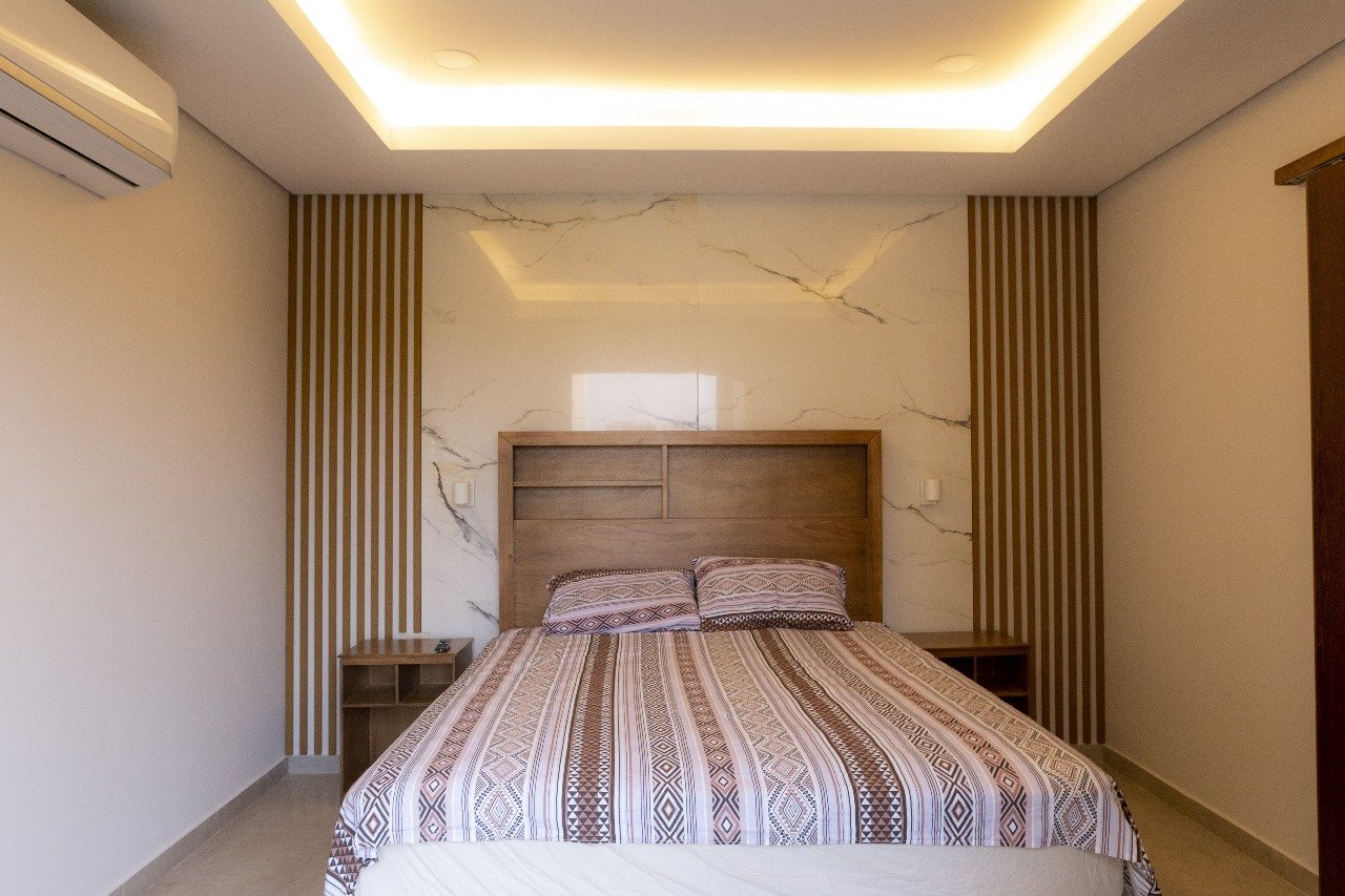 Dormitorio principal con cabecera de marmol y revestimiento de listones de madera, vivienda Aqua Village - OGA Constructora