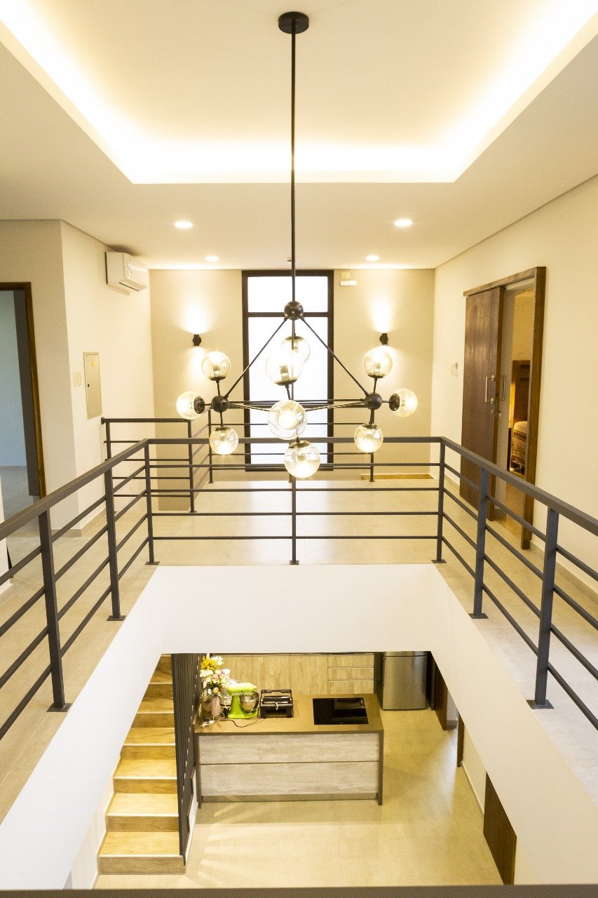 Hall de doble altura con escalera y arana de luces negra, interior de vivienda moderna Aqua Village - OGA Constructora