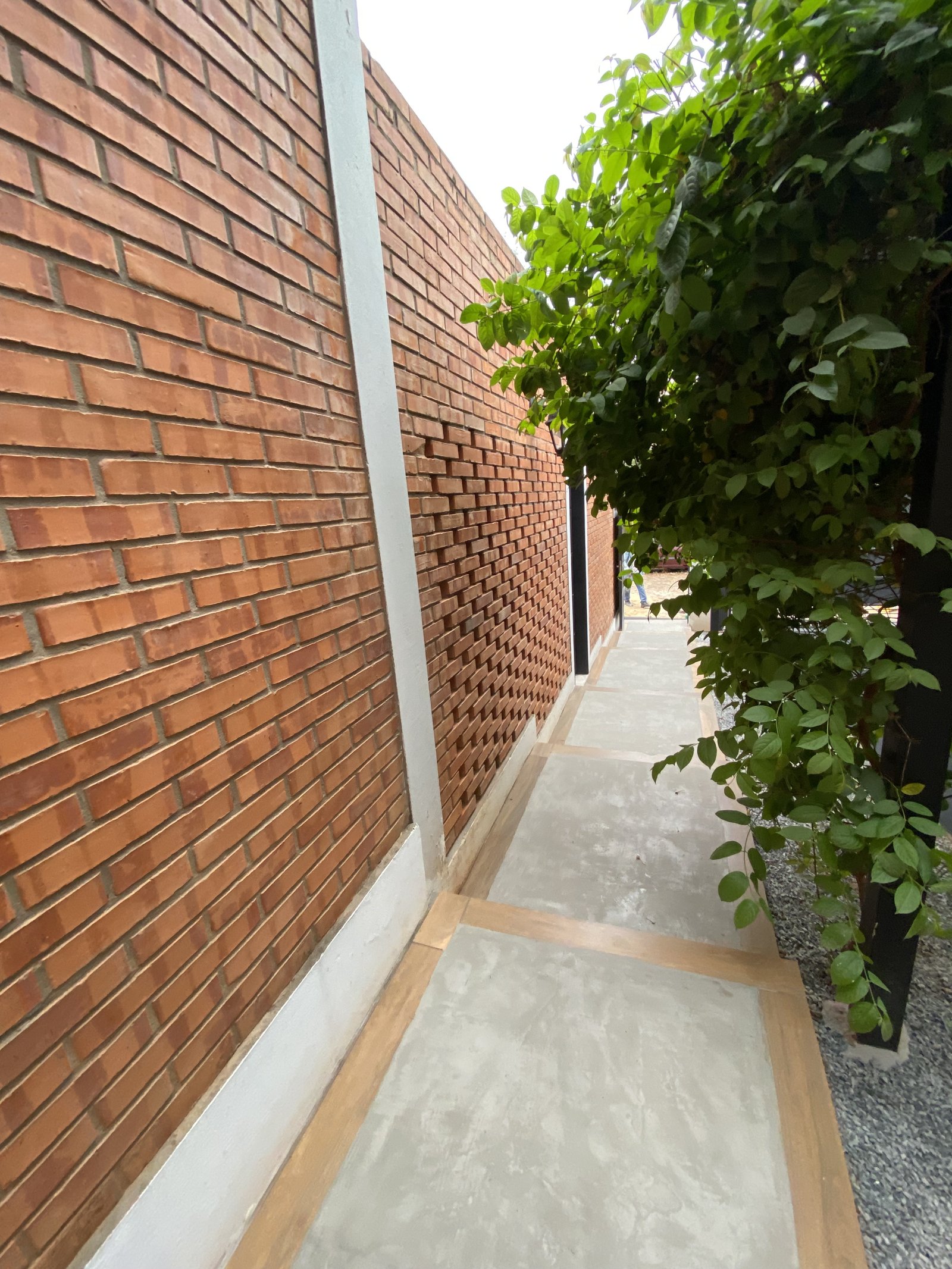 Pasillo lateral entre muro de ladrillo y muro gris de la vivienda - OGA Constructora